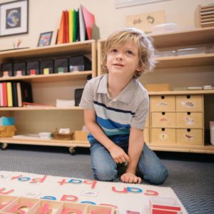 Child sitting on ground smiling and creating words with letters